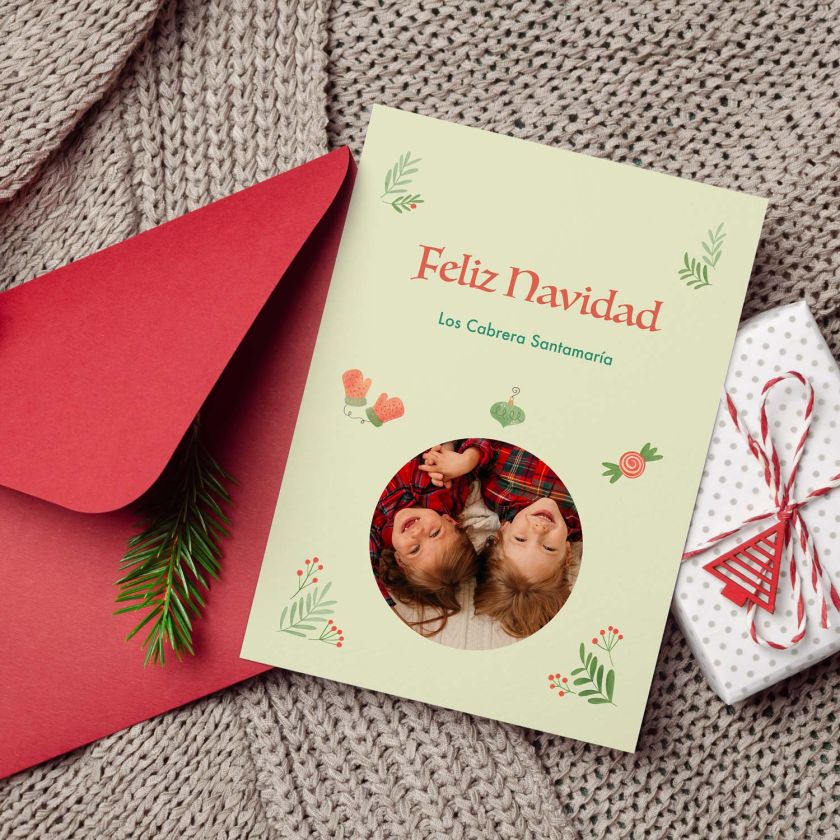 mockup de tarjeta navideña con foto infantil junto a sobre rojo y decoración navideña
