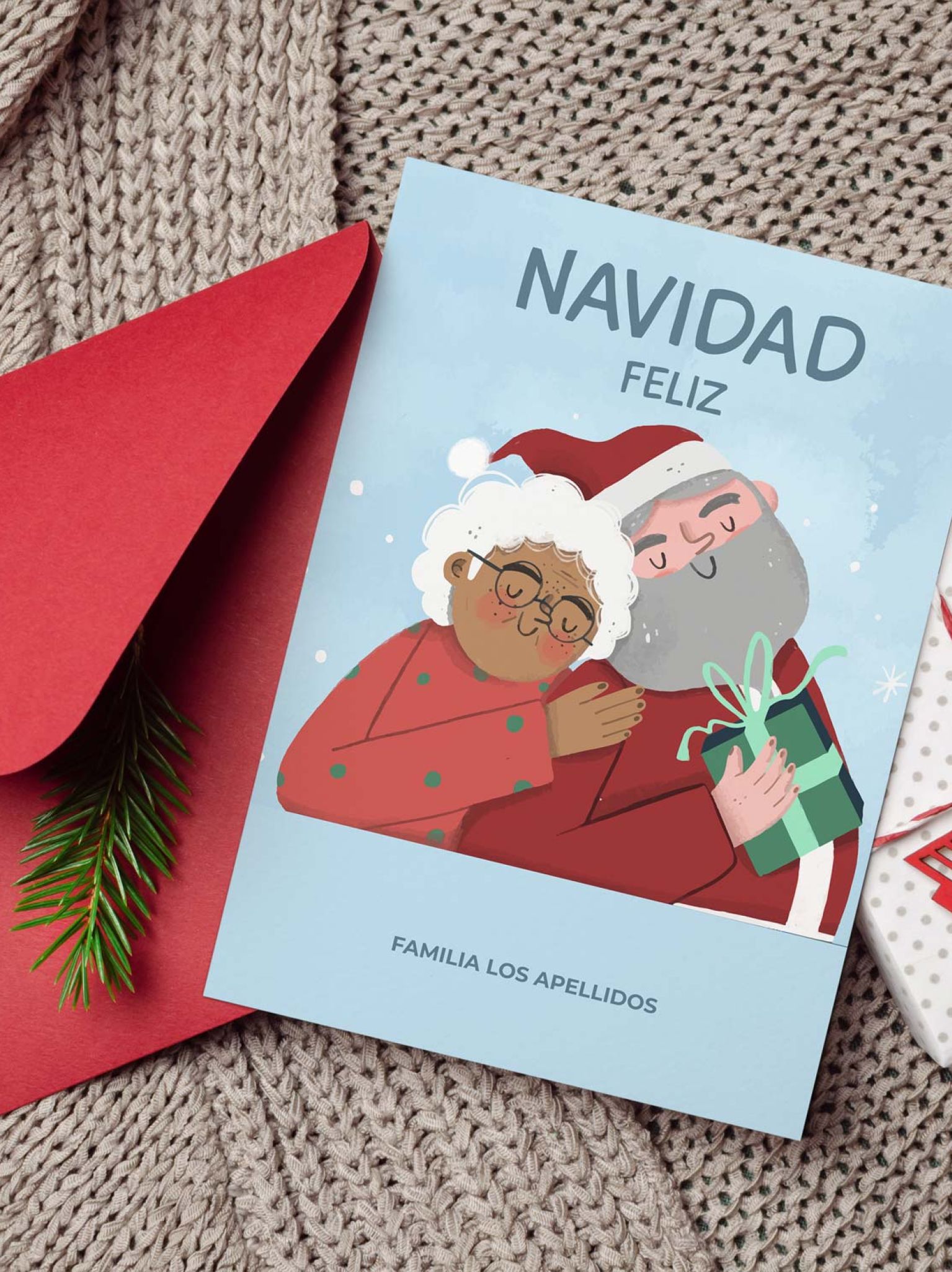 Tarjeta navidad personalizada con Papá Noel y señora Claus junto a sobre rojo y decoración