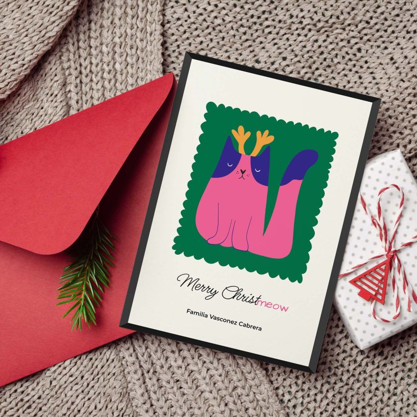 Tarjeta de Navidad con ilustración de gato rosado con cuernos, personalizada con apellidos, junto a sobre rojo y paquete de regalo
