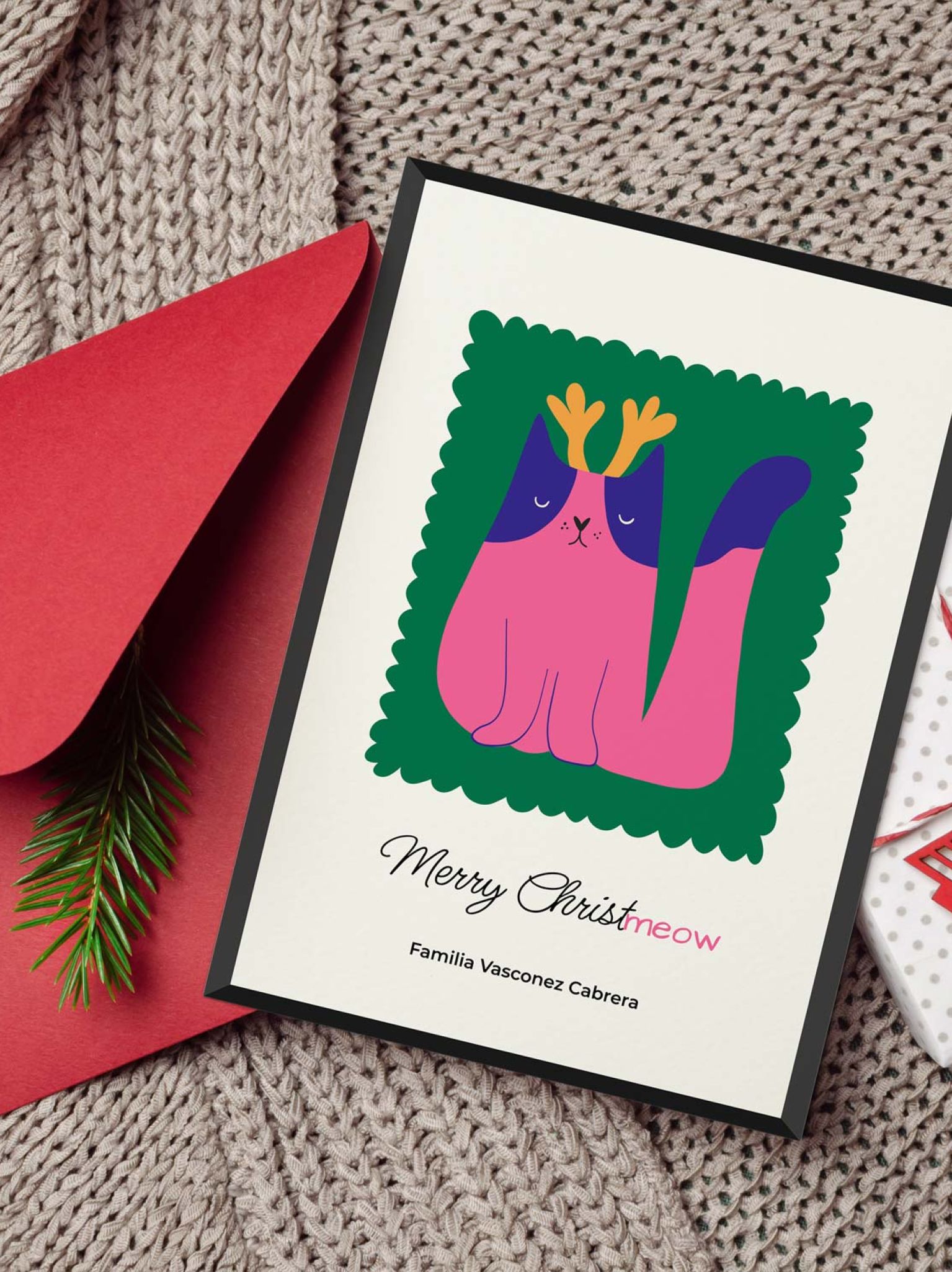 Tarjeta de Navidad con ilustración de gato rosado con cuernos, personalizada con apellidos, junto a sobre rojo y paquete de regalo