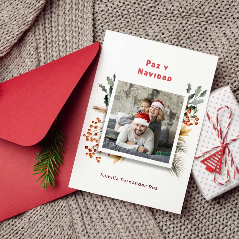 tarjeta navidad con foto personalizada colocada junto a sobre rojo y regalo navideño
