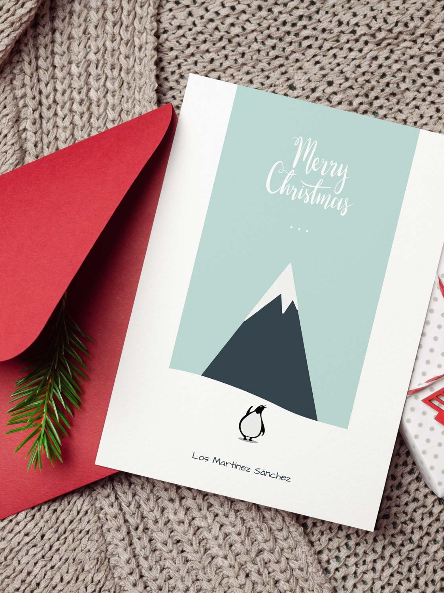 Tarjeta navideña personalizada con pingüino junto a sobre rojo, rama de pino y regalo navideño