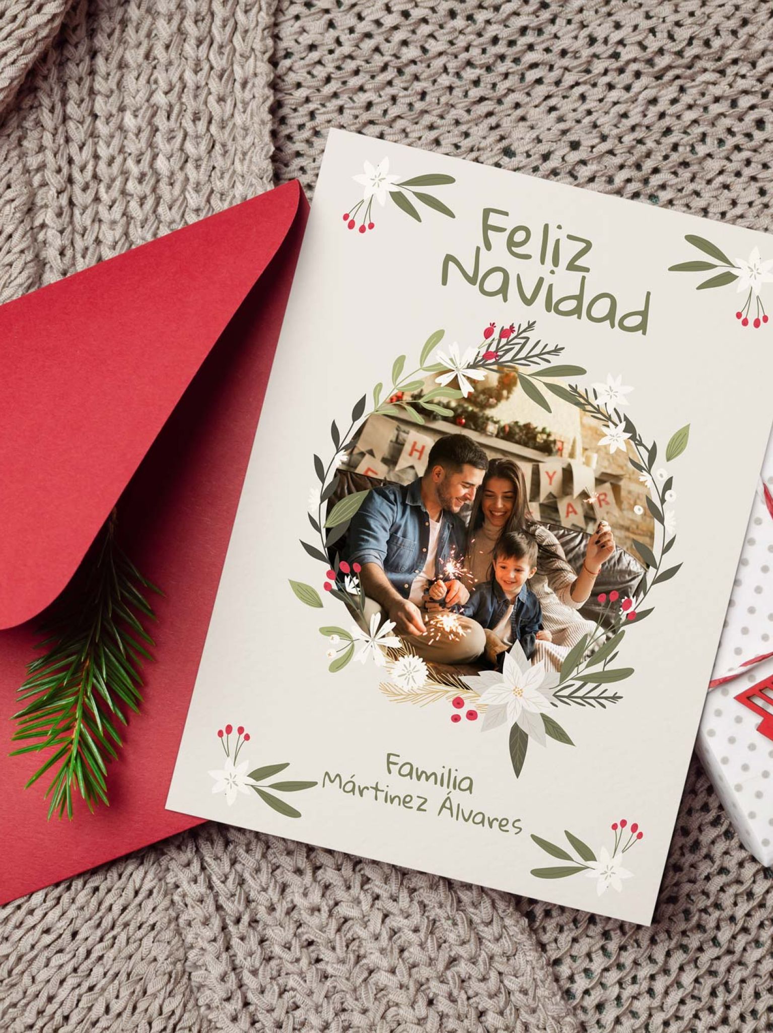 Mockup de tarjeta navide&ntilde;a con foto personalizable colocada junto a sobre rojo y decoraci&oacute;n navide&ntilde;a