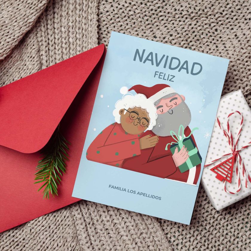 Tarjeta navidad personalizada con Papá Noel y señora Claus junto a sobre rojo y decoración
