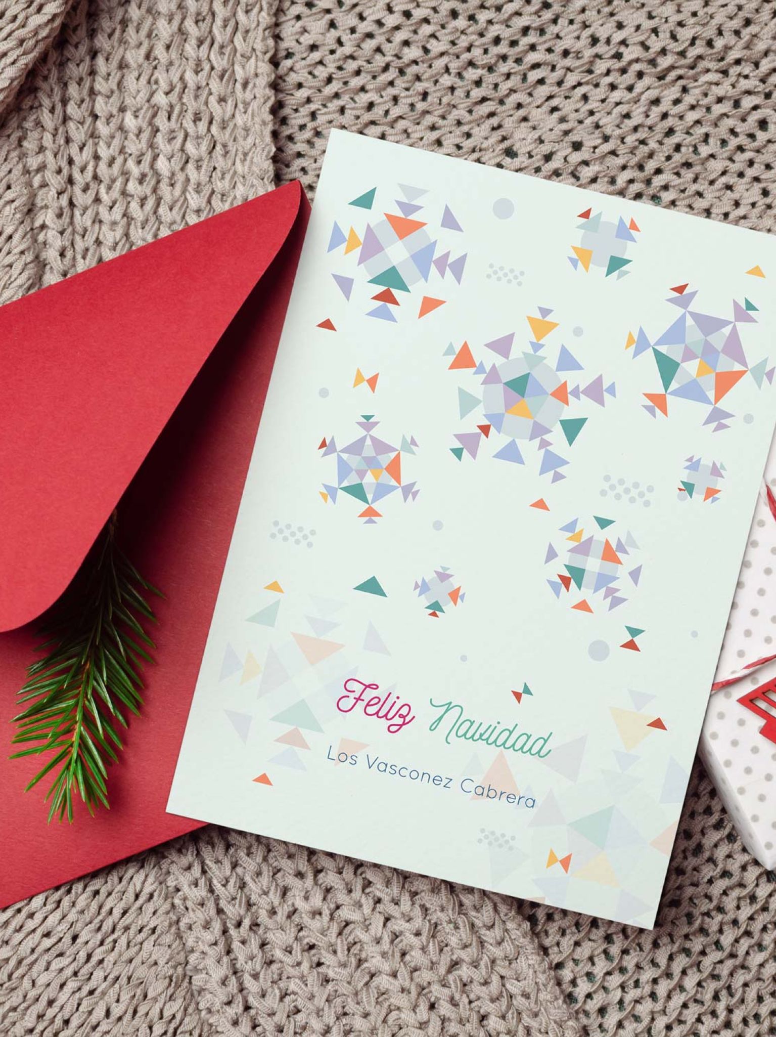 Tarjeta de Navidad personalizada con diseño geométrico y nombre de familia sobre fondo navideño con sobre rojo