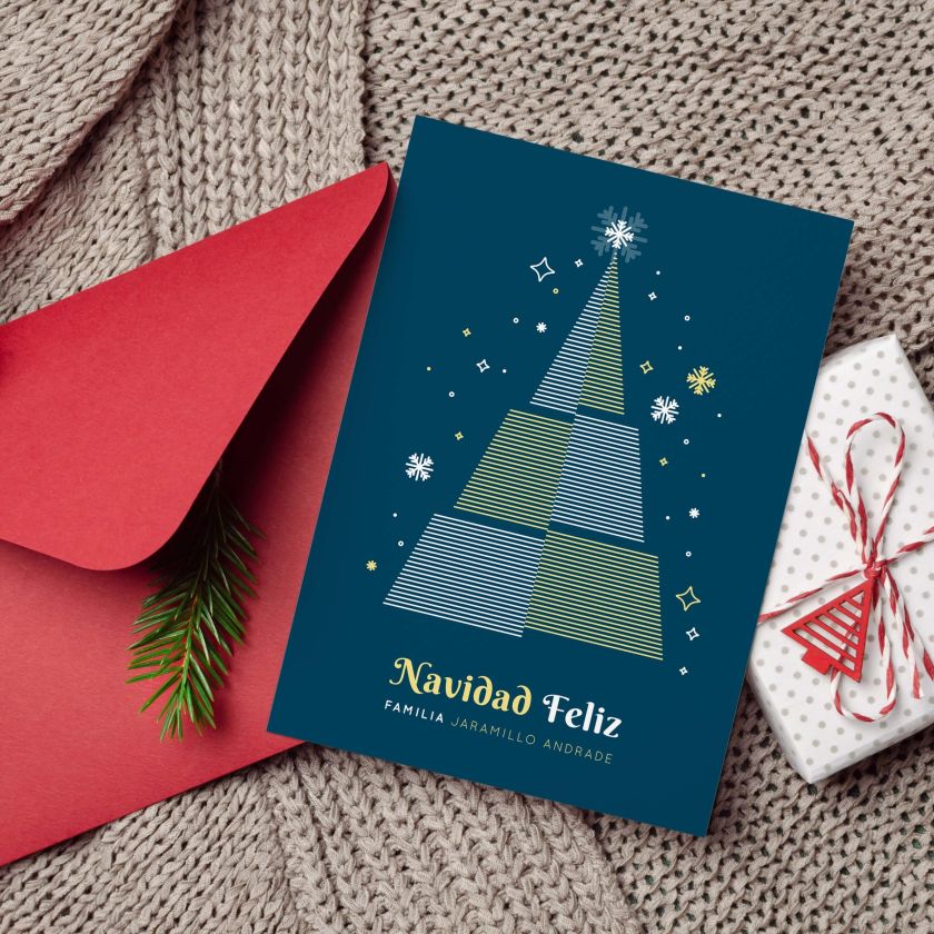 Tarjeta navideña personalizada azul con árbol y sobre rojo, acompañada de decoración navideña y regalo