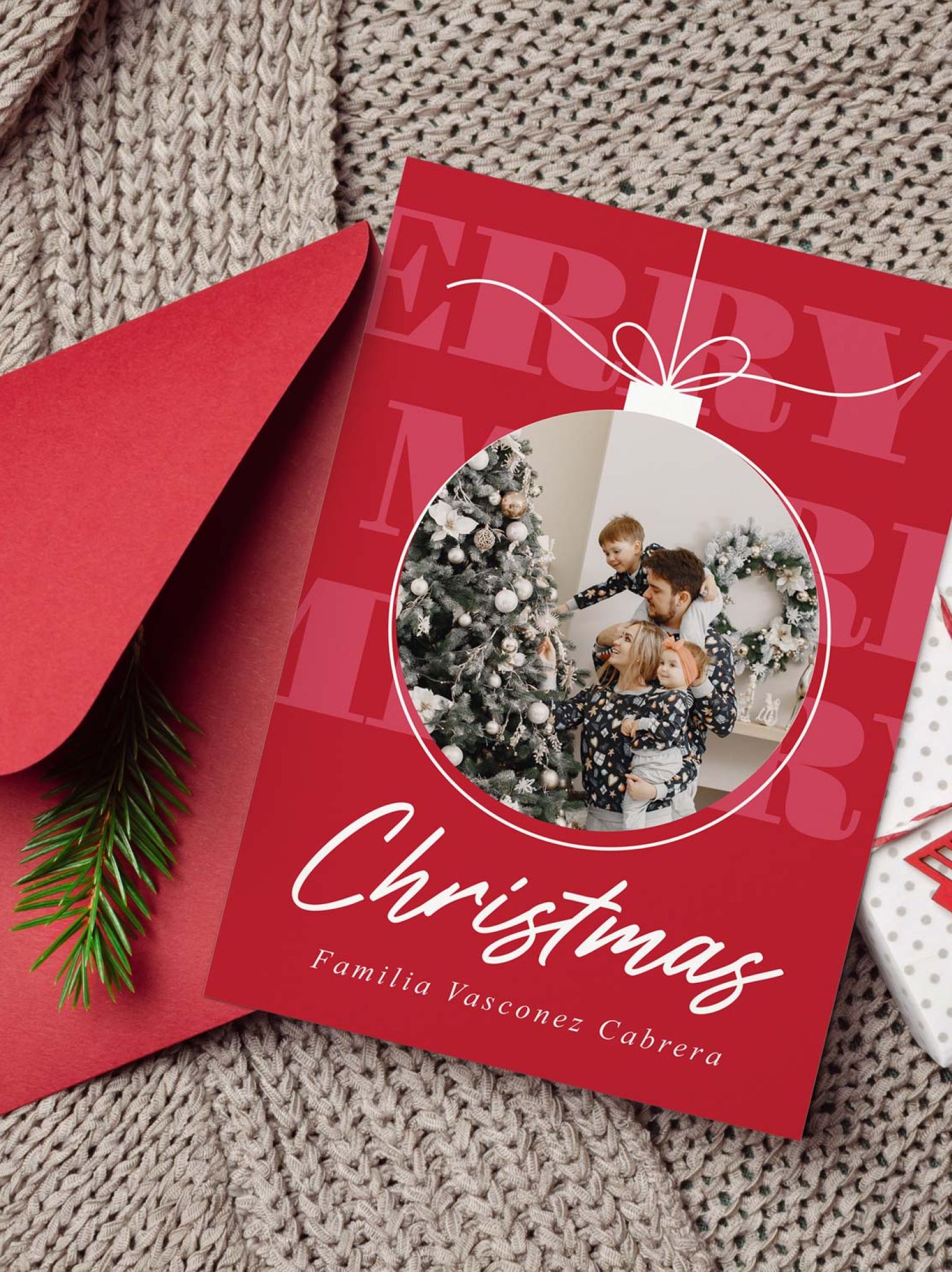 mockup de tarjeta con foto navide&ntilde;a junto a un sobre rojo un regalo y una manta tejida